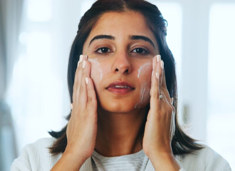 devojka crne kose nanosi kremu na lice
