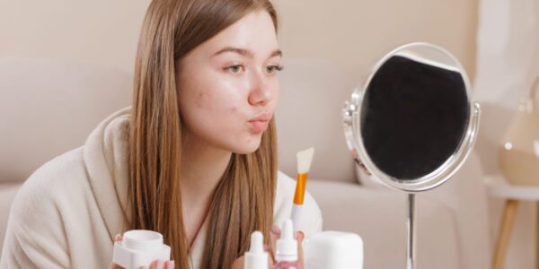 devojka se fleda u ogledalo i drži kremu za lice u ruci