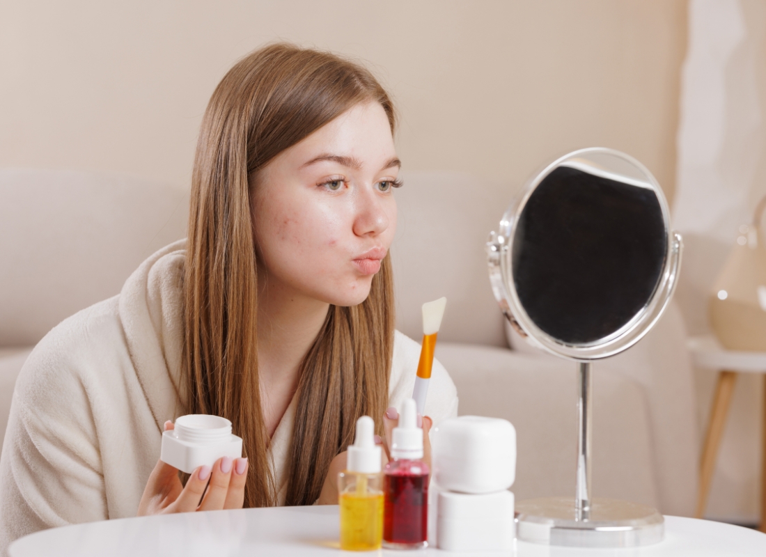 devojka se fleda u ogledalo i drži kremu za lice u ruci